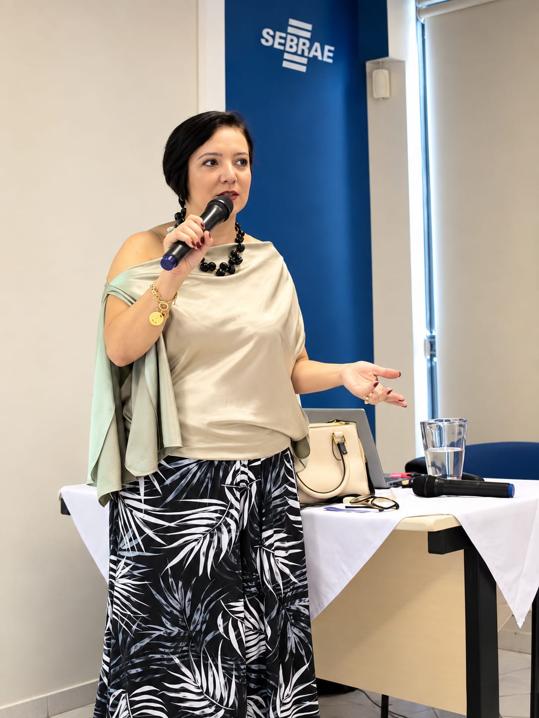 Lilian Lima palestrando no SEBRAE, com microfone na mão e logo do SEBRAE ao fundo